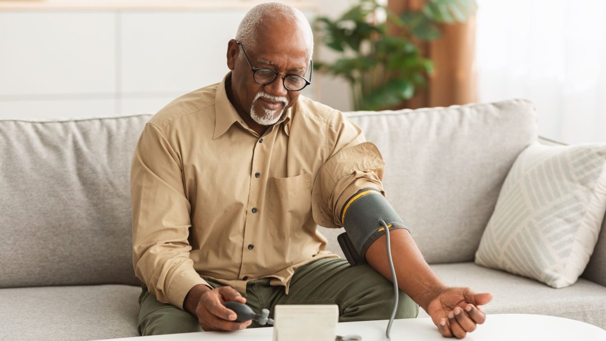 Man taking his blood pressure reading on sofa | Intus Healthcare