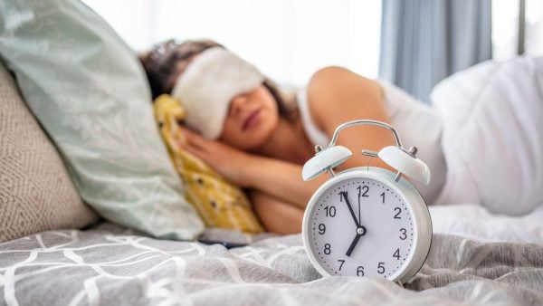 Woman in bed with eye mask on, alarm clock on bedside table | Intus Healthcare