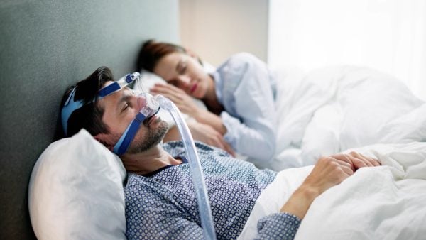 Man using a CPAP mask in bed beside woman | Intus Healthcare